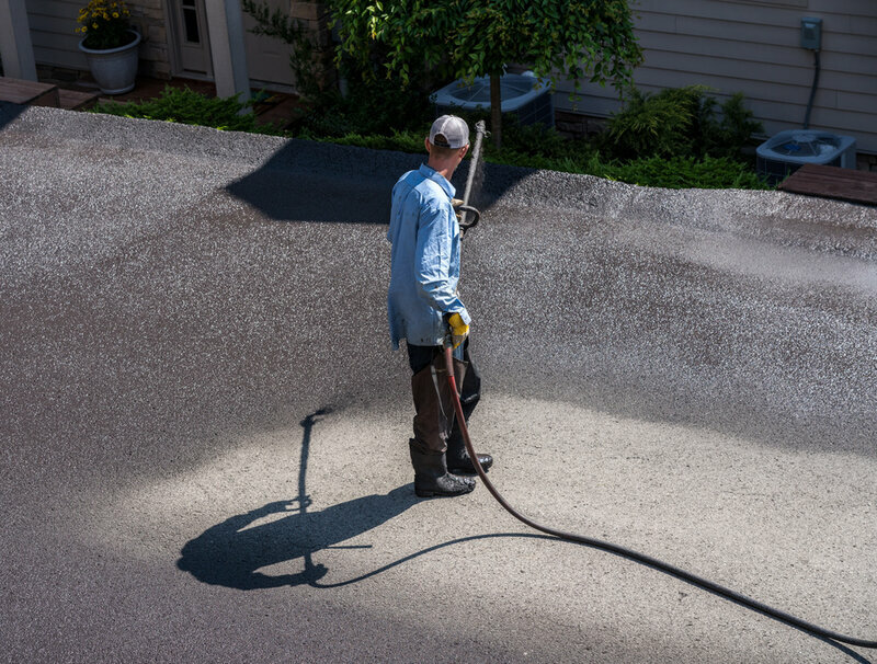 Workers spraying blacktop or asphalt sealer onto roadway