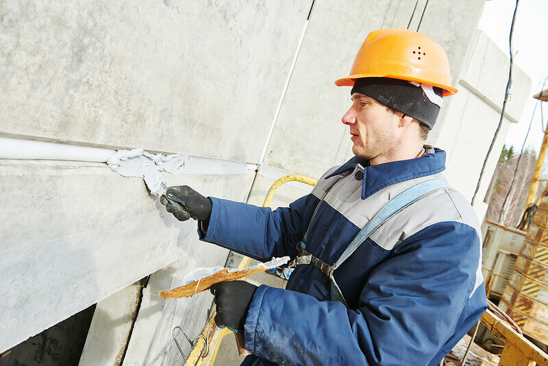 Facade plasterer sealing joint of building wall with putty